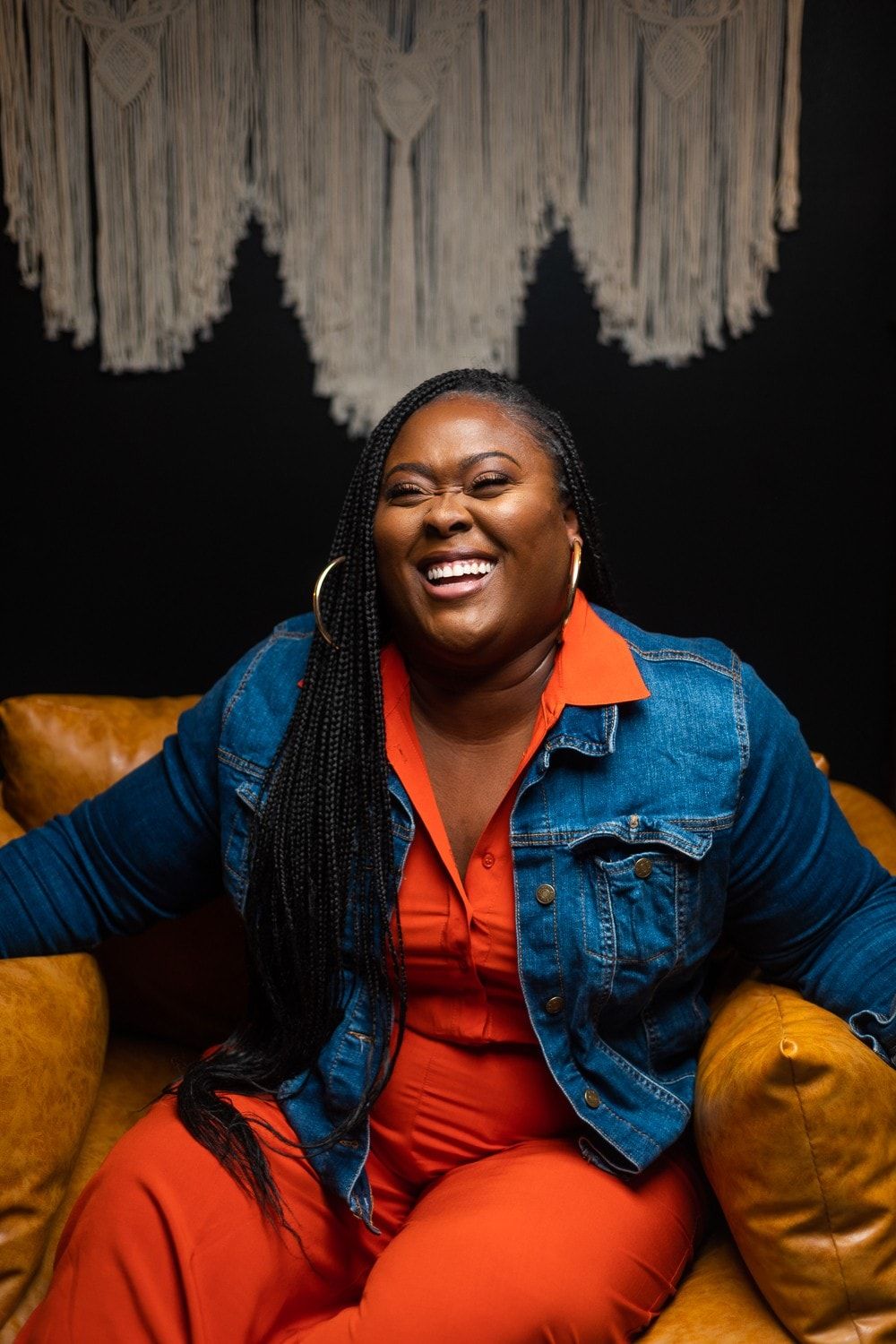 Ona laughing on a leather sofa in a denim jacket
