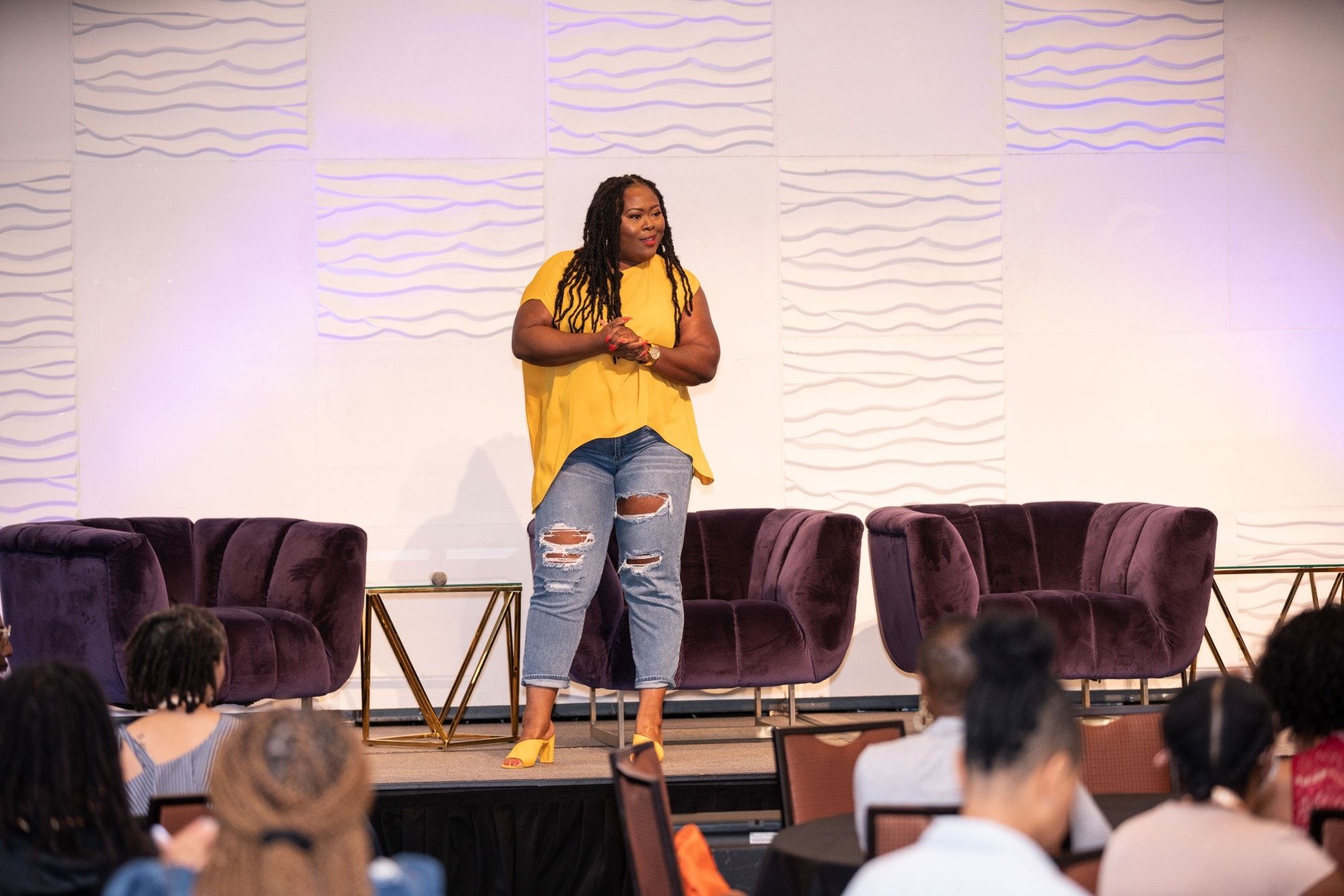 Ona Oghogho speaking on stage in a yellow top to a seated audience