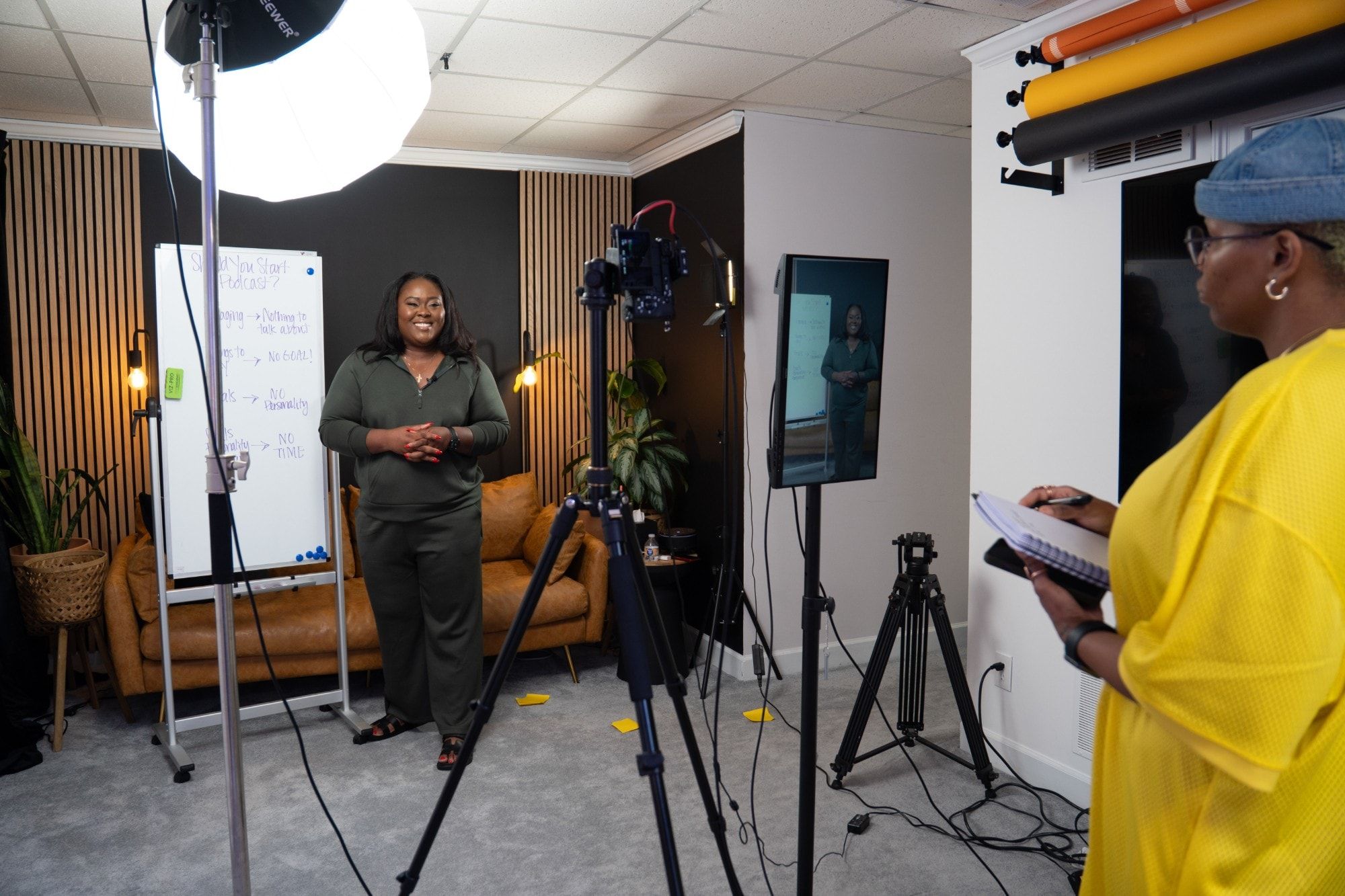 Ona on a production set in front of the camera while a crew member takes notes