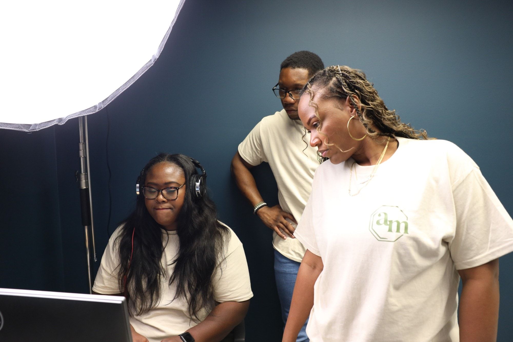 Ona at the editing desk in headphones with two Adode Media teammates looking on