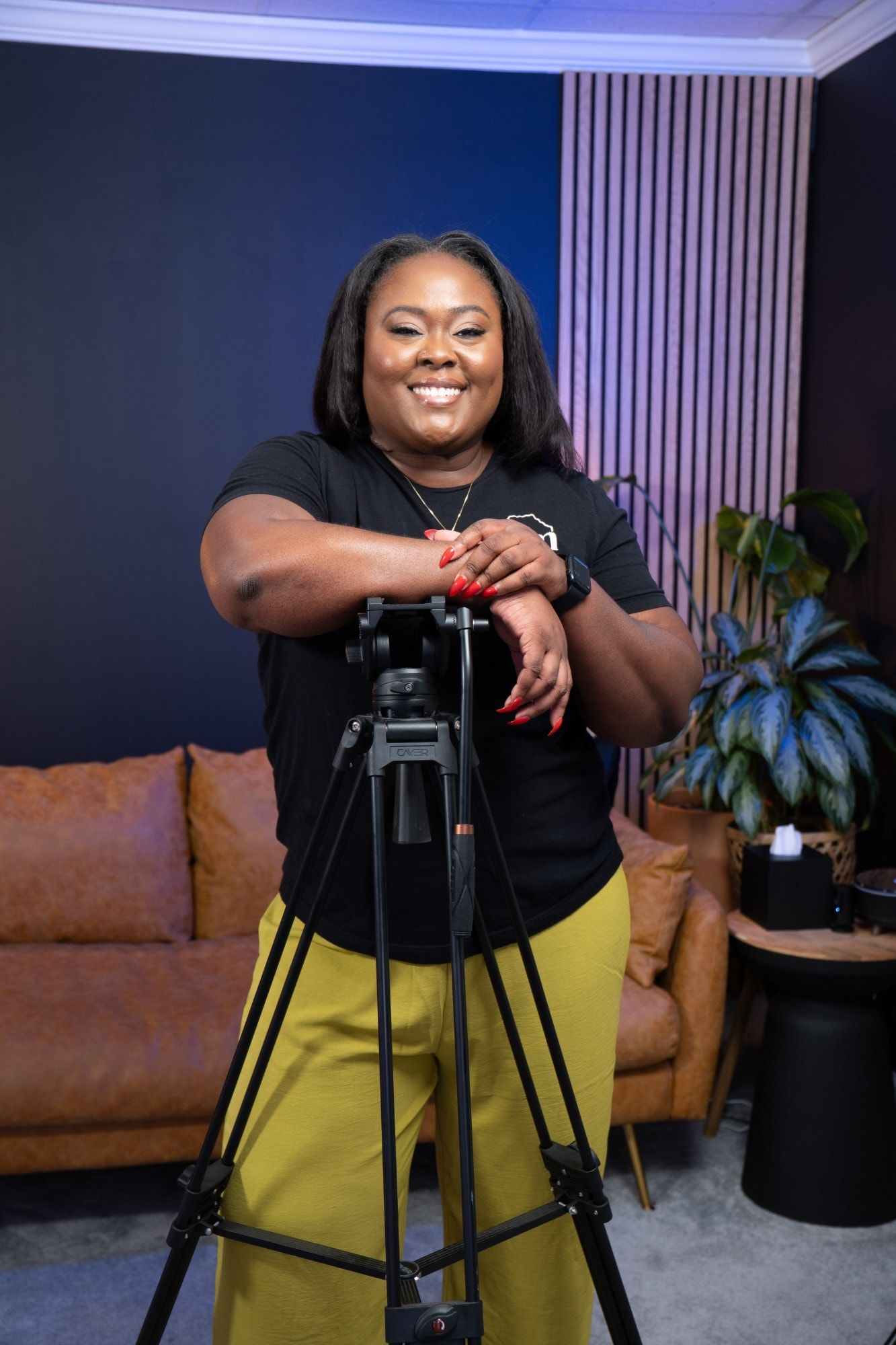 Ona smiling, leaning on a camera tripod in the studio