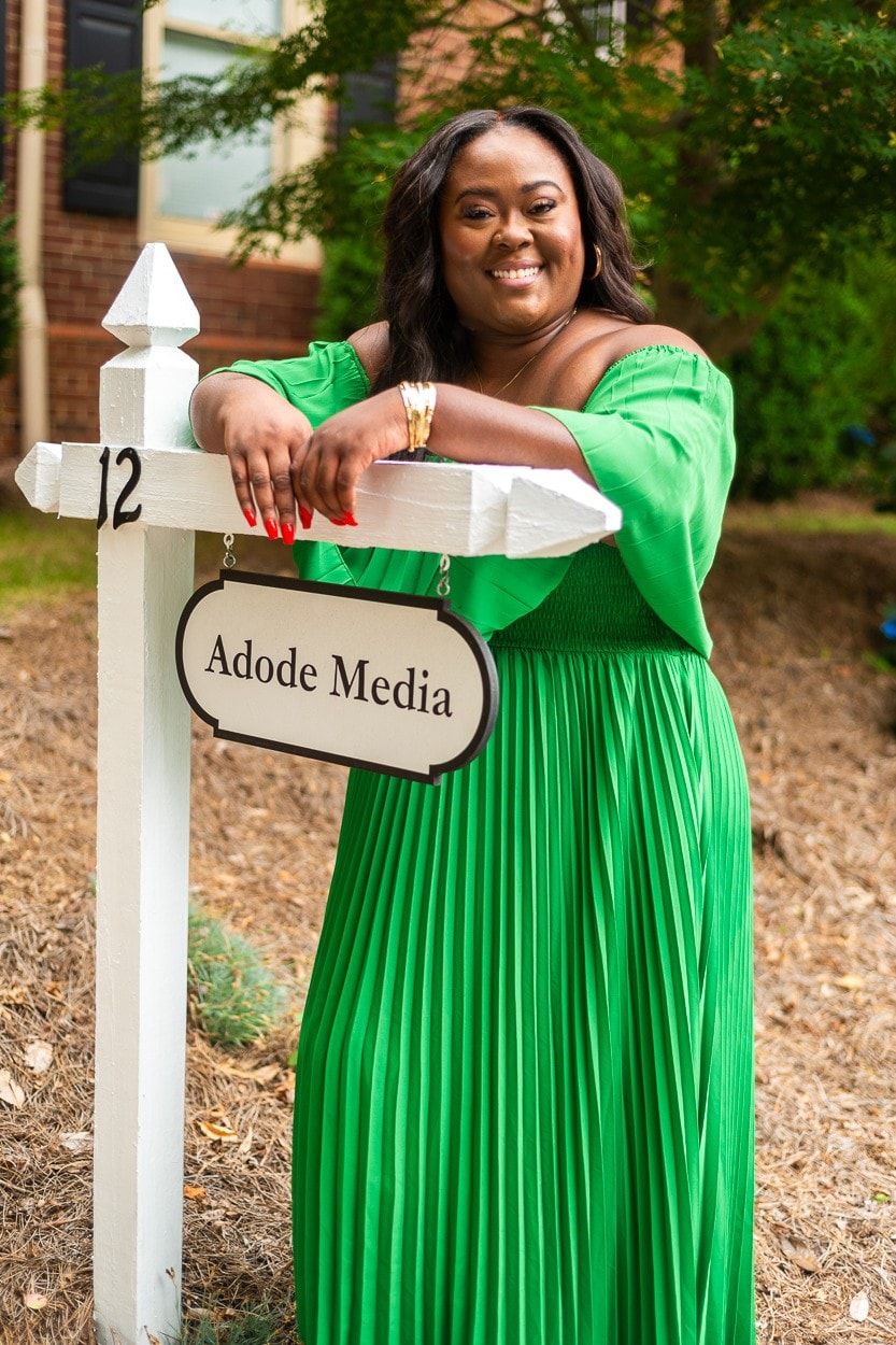 Ona in a green dress leaning on the Adode Media sign